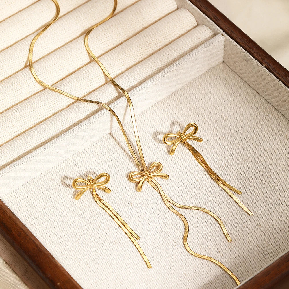 Gold jewelry with bow design on a textured beige surface